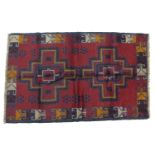 A Baluchi rug with red ground, two medallions in varying shades of blue, yellow and cream, with
