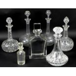 A group of seven glass decanters, comprising a simple, heavy rectangular whisky decanter, 12 by 7.