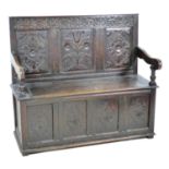 An 18th century oak settle, with carved frieze above a three panel carved back, open shaped