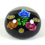 A Paul Ysart style paperweight, the black ground decorated with three flowers, the flowers, with