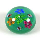 A Paul Ysart style paperweight, the green ground decorated with three flowers, with millefiore