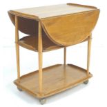 An Ercol elm and beech tea trolley, circa 1970, with drop leaves and three tiers, ball castors,