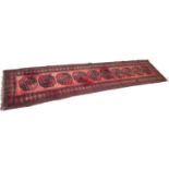 A Tekke rug with red ground, with central row of ten medallions, black decoration, 85 by 372cm.