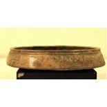 A shallow dish of bronze. It has Islamic writing around the outside and round an intricate pattern