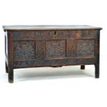 An 18th century oak chest, lift top over a three panel front carved with foliate patterns and