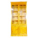 A modern pine bookcase, twin glazed doors, each with ten panes, enclosing four shelves, slide with