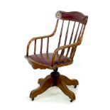 A late Victorian oak office / desk swivel chair, with shaped arms, red leatherette seat and
