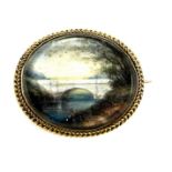 A Victorian yellow metal brooch, inset with painted plaque of figures beside a bridge, countryside