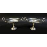 A pair of George V twin handled silver bon bon dishes, raised upon circular stepped bases, both