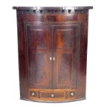 An early Georgian mahogany bow fronted corner cupboard, unusual feather banding to the frize and