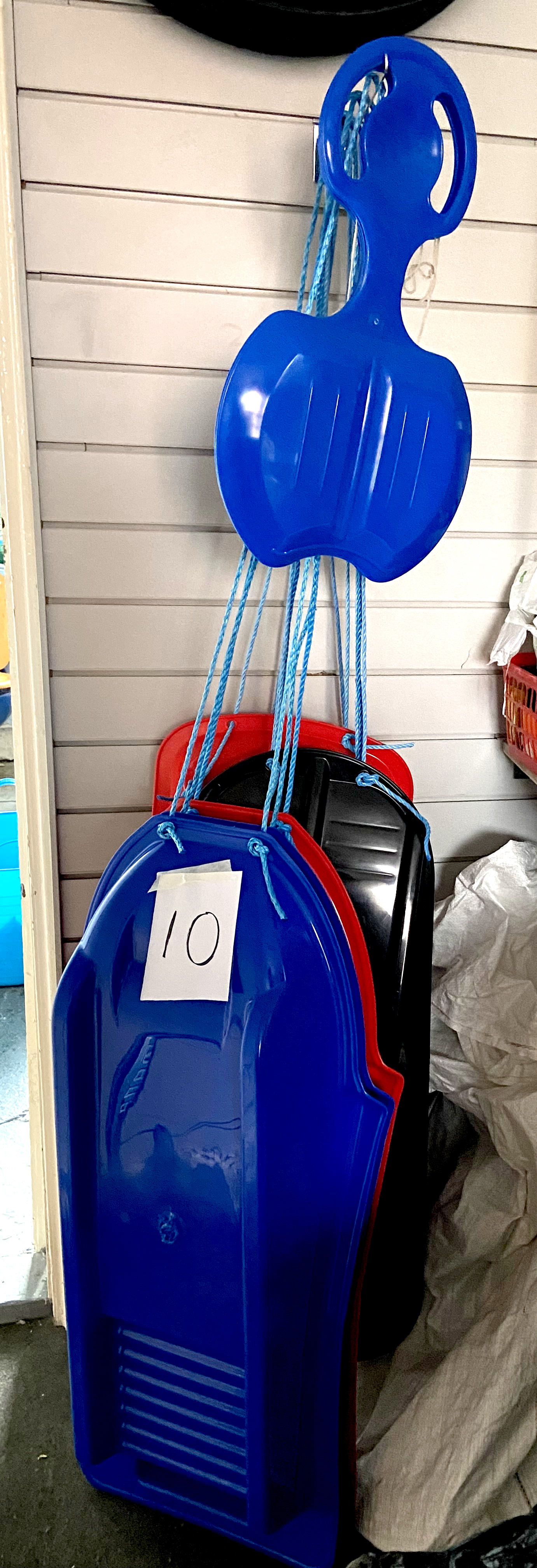 A group of six blue, red and black moulded plastic sledges, with blue rope pulls.