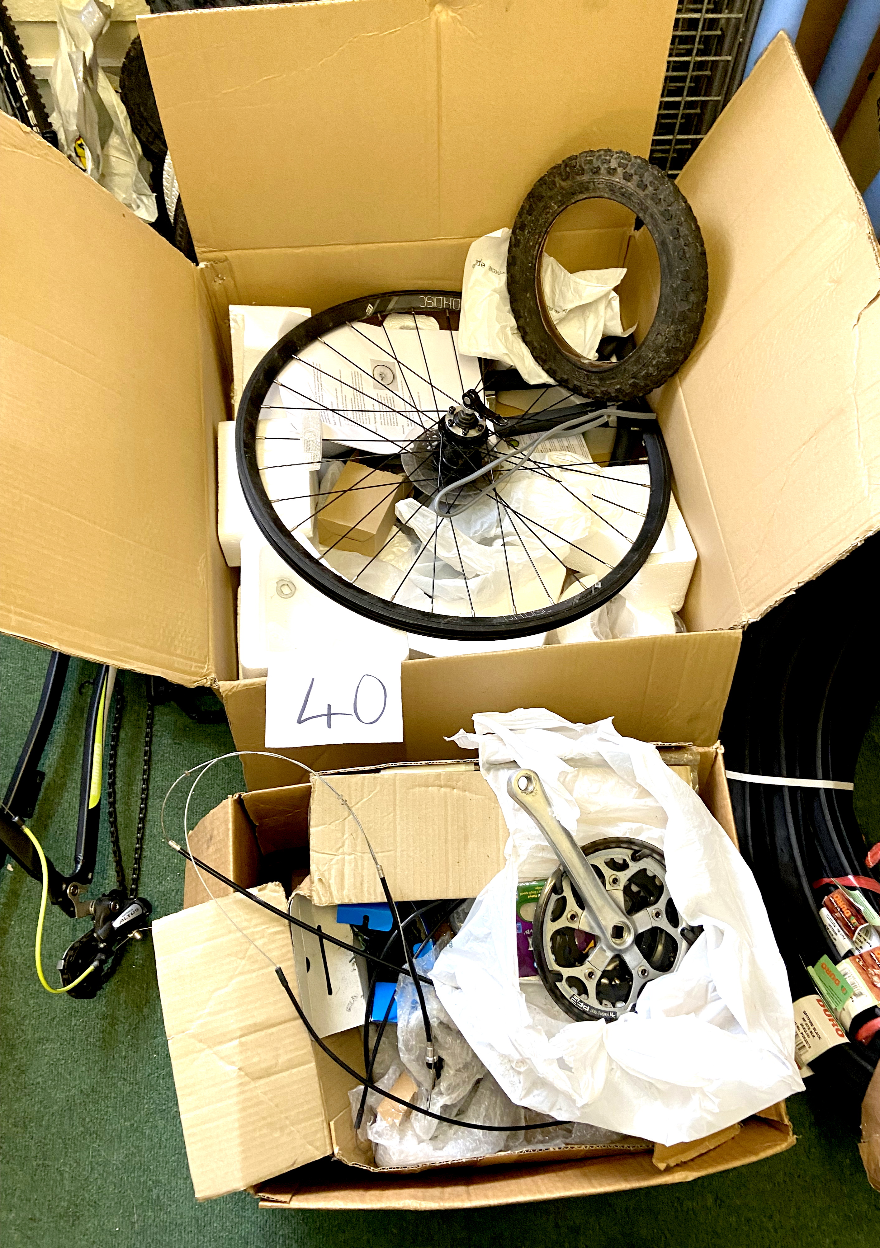 Two cardboard boxes containing a variety of bike parts, including a D.H.Disc wheel and rear gear