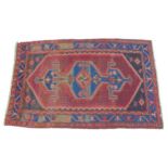 A red ground rug with blue borders, with central decorated with geometric shapes, 138 by 216cm.