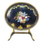 An Edwardian ebonised and painted papier mache oval tray table, the oval hinged surface decorated