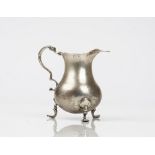 An early George III silver cream jug of baluster form having a shaped rim and raised on three pad