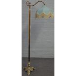 An early 20th century brass standard lamp, raised on a triform base with paw feet, with shade,