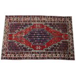 A Mazlaghan rug, Persian, the madder field with a serrated indigo medallion,