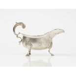 A late Victorian silver sauceboat having a shaped rim, scrolled handle and raised on three pad feet,