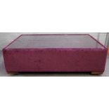 A large square plum coloured upholstered coffee table, with inset glass top on block supports,