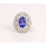 A white gold, tanzanite and diamond ring, claw set with the oval cut tanzanite within a...
