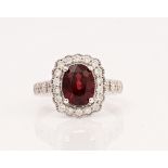 An 18ct white gold, red spinel and diamond cluster ring, claw set with the oval cut red spinel...