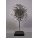 A modern slivered metal sun-burst sculpture on hardwood plinth base