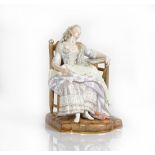 A Meissen figure of a lady, late 19th century, seated asleep in a chair, her left arm resting...