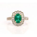A white gold, emerald and diamond oval cluster ring, claw set with the oval cut emerald in a...