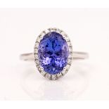 A white gold, tanzanite and diamond oval cluster ring, claw set with the oval cut tanzanite in...