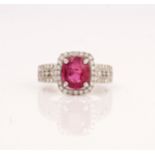 A white gold, ruby and diamond ring, claw set with the oval mixed cut ruby in a surround of...
