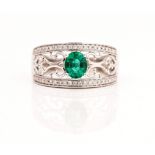 A white gold, emerald and diamond ring, claw set with the oval cut emerald between scroll...