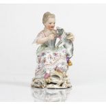 A Meissen figure of a seated girl, late 19th century, modelled holding a grey cat wearing a...