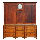 A George III oak housekeeper's cupboard with integral clock flanked by a pair of shaped panel...