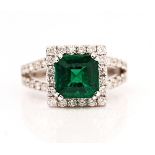 An 18ct white gold, emerald and diamond square cluster ring, claw set with the cut cornered...
