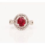 An 18ct white gold, ruby and diamond ring, claw set with the oval cut ruby in a surround of...