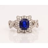 A platinum, sapphire and diamond cluster ring, claw set with the cushion shaped sapphire in a...
