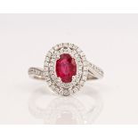 A white gold, ruby and diamond oval cluster ring, claw set with the oval cut ruby in a two...