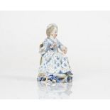 A Meissen figure of a girl, late 19th century, modelled seated holding a shuttle, painted...