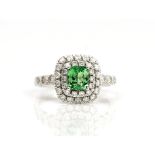 A white gold, tsavorite garnet and diamond cluster ring, claw set with the cushion shaped...
