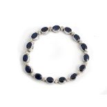 An 18ct white gold, sapphire and diamond bracelet, collet set with a row of oval cut sapphires...