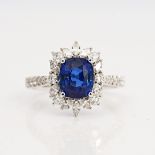 A white gold, sapphire and diamond cluster ring, claw set with the cushion shaped sapphire in...
