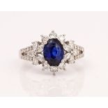 A platinum, sapphire and diamond cluster ring, claw set with the oval cut sapphire in a...