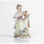 A Meissen figure of a seated girl, late 19th century, modelled holding a grey striped cat...