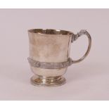 A silver christening mug, decorated with a Celtic style band and handle, raised on a circular...