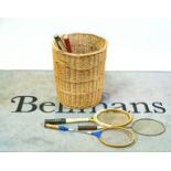 A wicker basket containing vintage tennis, badminton rackets and sundry.