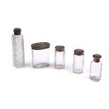 A SILVER TOPPED VICTORIAN GLASS SCENT BOTTLE AND FOUR SILVER TOPPED GLASS TOILET BOTTLES AND...