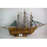 A large wooden scale model of a three masted sailing ship in full sail.