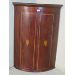A George III bow fronted inlaid mahogany corner cupboard with parquetry cornice over two doors each