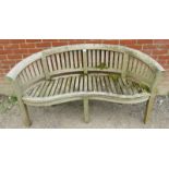 A nicely weathered teak garden bench with a shaped front and slatted seat & back rests, raised on