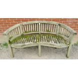 A nicely weathered teak garden bench with a shaped front and slatted seat & back rests, raised on